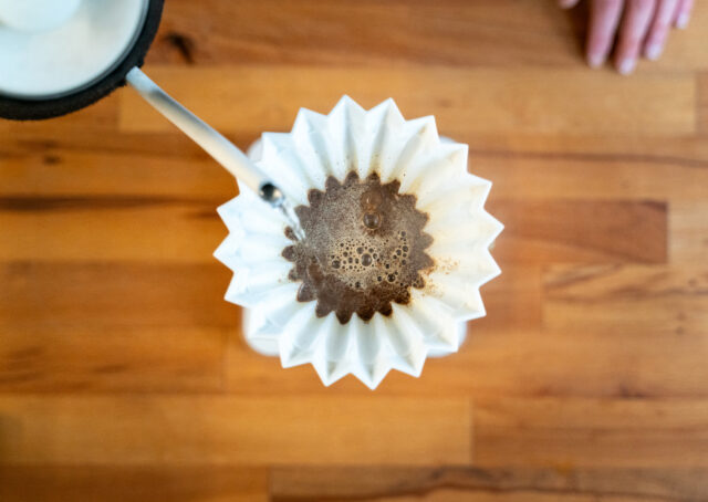Hot water being poured into a pour-over container, seen from above, as the coffee grounds are blooming.